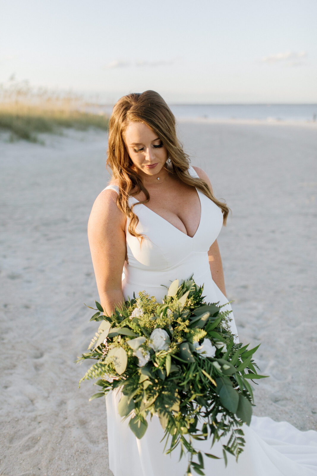 bride looking down at bouquet on beach