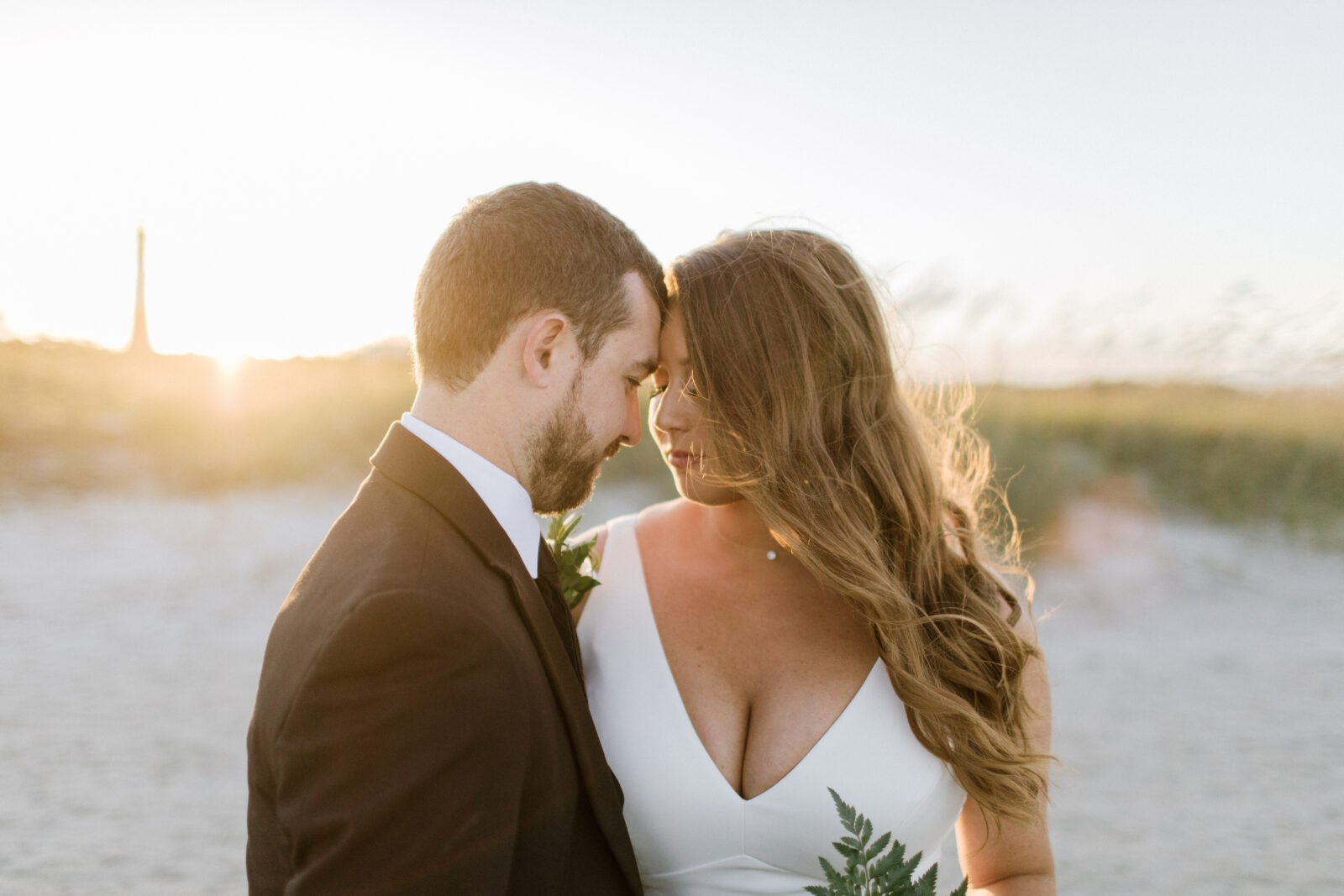 bride and groom touch foreheads standing on beach at sunset