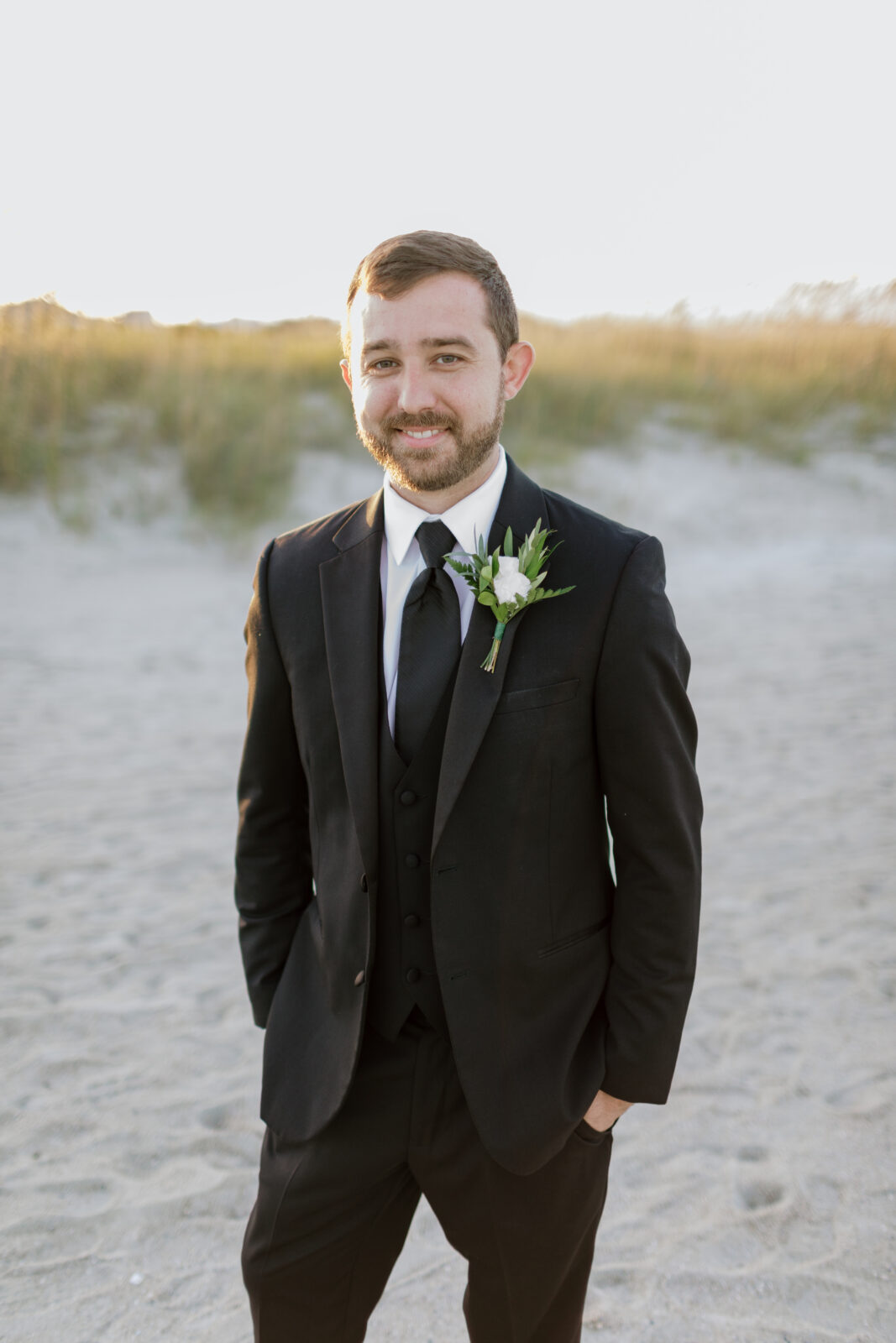groom in black tux and greenery boutonniere smiling at camera