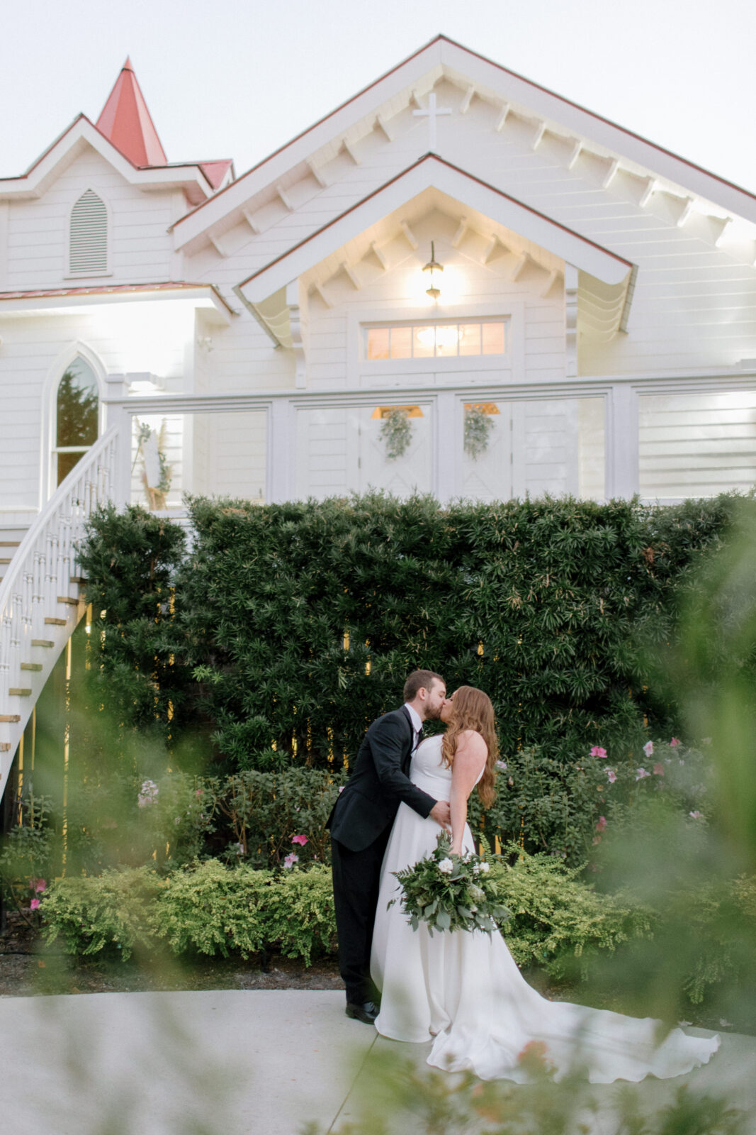 groom dips bride in front of greenery fencing and tybee island wedding chapel