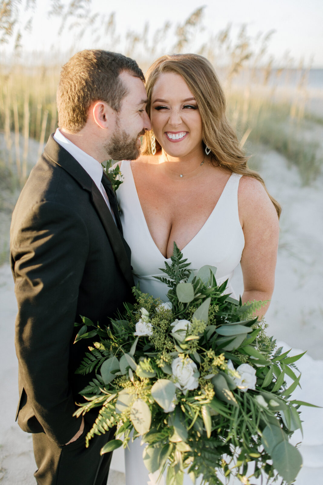 groom kisses bride over ear and bride smiles holding bouquet